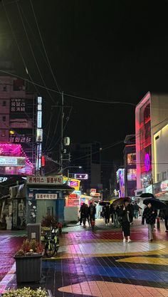 many people are walking down the street in the city at night with their umbrellas open