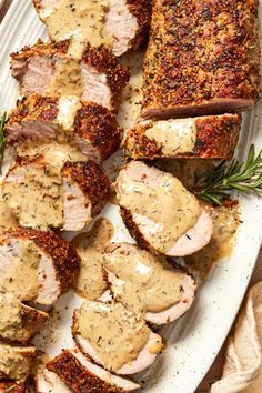 sliced pork with gravy on a white platter next to bread and sprig of rosemary