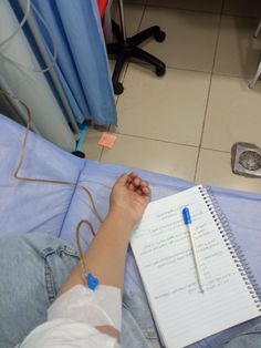 a person sitting on the floor with a notebook and pen in their hand, next to a hospital bed