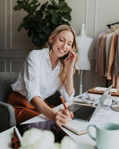 a woman sitting at a desk talking on the phone and working on her laptop computer