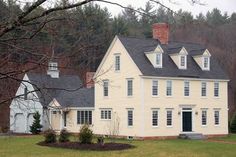 a large white house sitting in the middle of a lush green field next to a forest