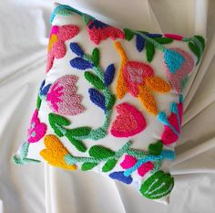 a white pillow with multicolored flowers on it sitting on top of a bed