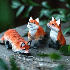 three little figurines of foxes sitting on a wooden table next to green leaves