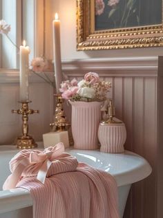 a bathtub with pink towels and candles in the corner, next to a painting on the wall