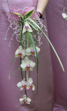 a woman in a pink dress holding a bouquet of white orchids and greenery