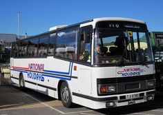 a white bus parked in a parking lot next to another bus with people on it