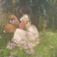 a woman sitting in the grass with a basket full of flowers