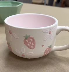 two cups sitting on top of a table next to each other with strawberries painted on them