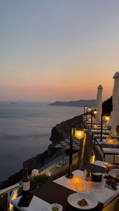 an outdoor dining area overlooking the ocean at dusk with candles lit on tables and chairs