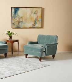 a living room with two blue chairs and a rug in front of a painting on the wall