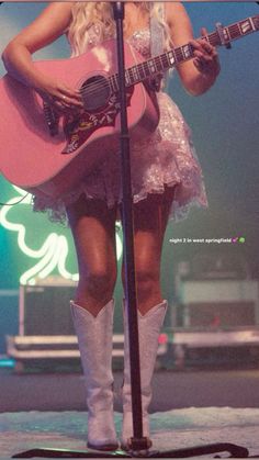 a woman in white boots holding a pink guitar and singing into a microphone on stage