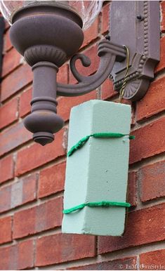 a green wrapped present hanging from a brick wall next to a light fixture on the side of a building