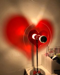 a red heart shaped lamp sitting on top of a table next to a white wall