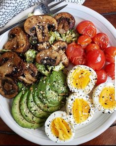 a white plate topped with eggs, tomatoes and cucumbers next to sliced avocado