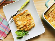 a white plate topped with lasagna next to a green and yellow fork on top of a wooden table