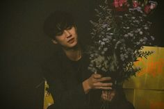 a young man holding a bouquet of flowers in front of a yellow sign that reads,