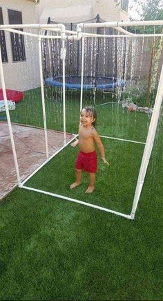 a little boy standing in front of a soccer goal on top of green grass next to a house