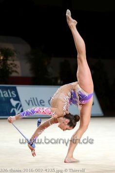 a woman doing a handstand on top of a pole in an indoor arena