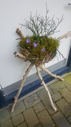 a planter made out of branches and twigs with purple flowers in it on the side of a building