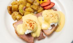 a white plate topped with ham, potatoes and gravy next to strawberries