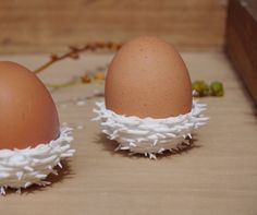 two brown eggs with white feathers sitting on top of a wooden table next to each other