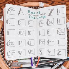 an open notebook sitting on top of a basket filled with markers and pencils next to pens