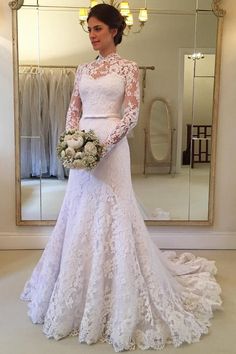 a woman standing in front of a mirror wearing a white wedding dress and holding a bouquet