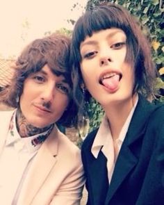 two young men posing for a photo in front of a bush with their tongue out