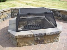 a fire pit sitting on top of a brick patio next to a stone wall and grass