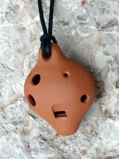 a clay piece with holes in the middle on a black cord attached to a stone wall