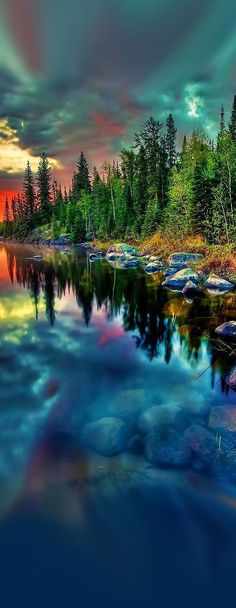 an image of a lake that is surrounded by trees and rocks with the sun setting in the background