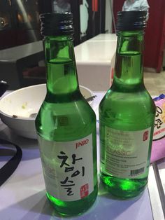 two green bottles sitting next to each other on top of a white countertop in front of a bowl