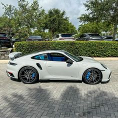 a white sports car is parked in front of some bushes and trees with blue rims