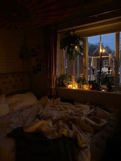 an unmade bed sitting in front of a window with candles on the windowsill