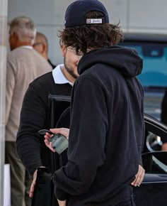 a man in a black hoodie standing next to a car