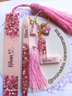 two personalized keychains with tassels on top of it and a pink ribbon