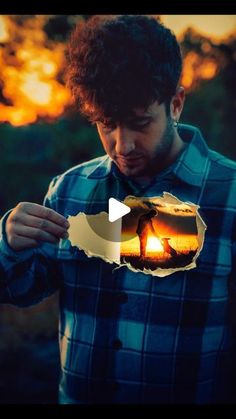 a man looking down at his cell phone while the sun is setting in the background