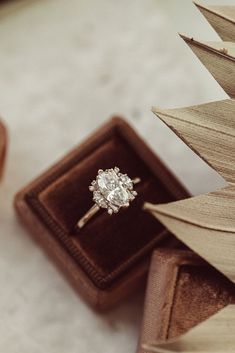 an engagement ring sitting in a box on top of a wooden table next to a plant