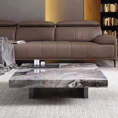 a marble coffee table sitting in front of a brown couch and bookshelf behind it