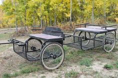 an old fashioned bike is parked in the grass near some trees and dirt, with one wheel attached to it's back end