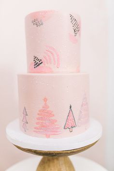 a pink and gold christmas cake on top of a white pedestal with trees painted on it