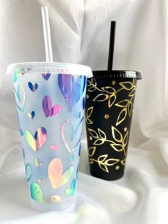 two different colored cups with straws in them on a white cloth covered tablecloth