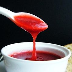 a spoon full of red liquid being poured into a white bowl with bread on the side