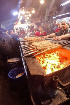 a man cooking food on top of a grill in a kitchen next to other people