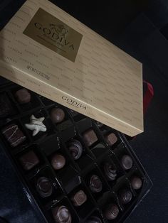 a box of assorted chocolates sitting on top of a black table next to a red ribbon