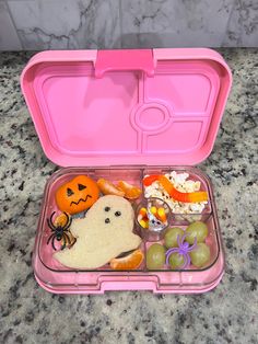 a pink plastic lunch box filled with halloween food and decorations on top of a marble counter