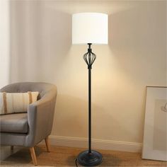 a floor lamp with a white shade on it in a room next to a chair