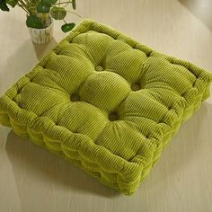 a green cushion sitting on top of a wooden table next to a vase with flowers