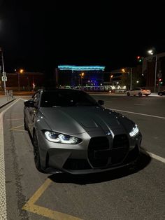 a silver car parked on the side of a road at night with buildings in the background