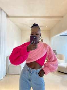 a woman taking a selfie with her cell phone in front of the camera wearing a pink sweater and jeans